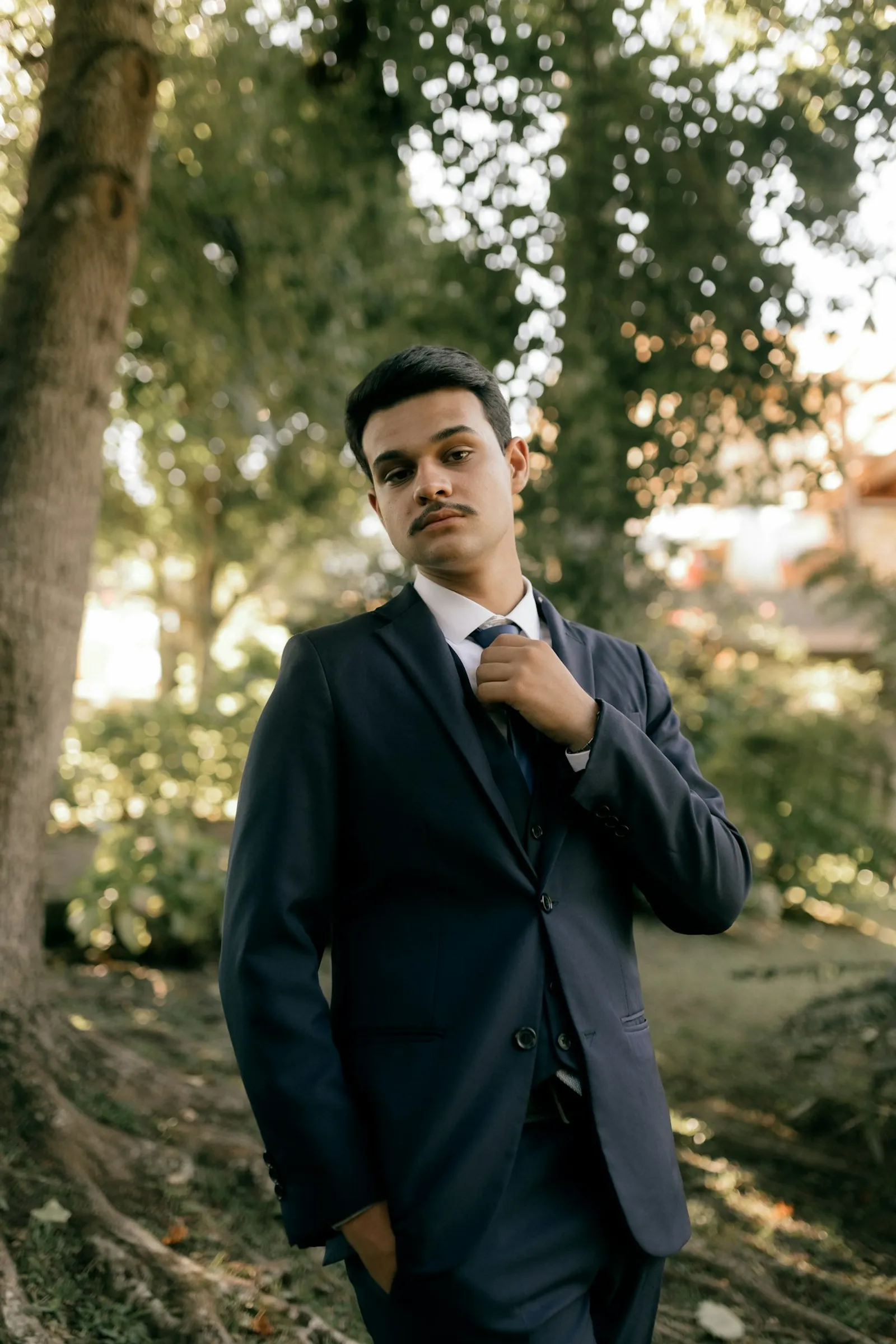 Mire în costum bleumarin ajustându-și cravata în grădină, înainte de ceremonie